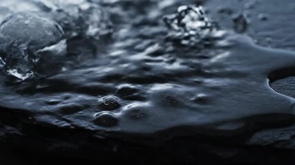 Wall Mural - Ice formations fluidly melt and transform into flowing water droplets on a dark, textured surface, showcasing a time-lapse of change science, drip, natural phenomena