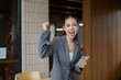 © amnaj - Young Asian businesswoman cheering and raising fist, feeling excited and happy after achieving success using a mobile phone