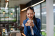 © amnaj - Asian businesswoman smiling, holding a cup of coffee or tea during a work break in a contemporary office environment