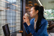 © amnaj - Asian businesswoman enjoying a coffee break, holding a ceramic cup, looking thoughtfully out a large office window