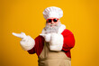 © deagreez - Funny Santa Claus in chef hat and apron with sunglasses posing on a yellow background showing a cheerful gesture