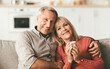 © Prostock-studio - Happy Long-Lasting Marriage. Older Husband Hugging Wife While She Holding Cup Of Coffee, Posing Smiling To Camera Sitting On Couch At Home. Retirement Lifestyle And Happiness