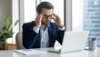 © Fauzan - A tired and stressed businessman sitting alone at his office desk, staring at his laptop with a worried expression.