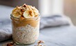 © simba kim - close up photo of a glass jar filled with creamy high protein peanut butter overnight oats topped with sliced banana crunchy nuts and a drizzle of peanut butter captured by a smartphone in natural mor