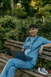 © La Famiglia - Female medical worker in scrubs using a laptop on a park bench
