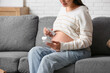 © Pixel-Shot - Young pregnant woman with fetal doppler listening to baby's heartbeat on sofa at home