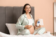 © Pixel-Shot - Young pregnant woman with fetal doppler listening to baby's heartbeat on bed at home