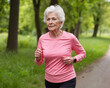 © lulla by - Elderly woman with determined mood, jogging on forest path, against lush green background
