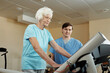 © pressmaster - Elderly Caucasian woman walking on treadmill under control of nursing assistant while getting through physical therapy in rehab hospital