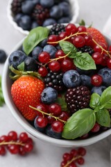 Wall Mural - Different ripe berries and basil leaves in bowl on light grey table, closeup