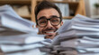 © photo for everything - Man surrounded by paperwork smiles. He wears glasses. The background is blurred. He seems to be up to his neck in work but he seems to be happy with it.