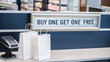 © Margo Miro - Buy one get one free promotion sign displayed at checkout with white shopping bags