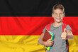 © New Africa - Little boy with backpack and stationery showing thumbs-up against flag of Germany. Language school