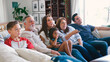 © Monkey Business - Multi-Generation Family Sitting On Sofa At Home Watching TV Together