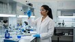 © OlgaNeuroArt - A female scientist in a lab coat and goggles analyzes a blue liquid in a test tube. A researcher working on a medical experiment in a modern laboratory. Women in STEM concept