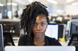 © Azhorov - Focused African American woman sits at office desk with computers. Serious expression reflects professionalism in daytime setting.