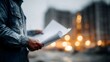 © Thares2020 - Architect reviews blueprints at an outdoor construction site with blurred lights in the background