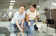 © JackF - Two friendly young adult sisters choosing dining table in furniture store, examining with interest display samples and discussing design and features
