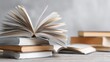 © The Little Hut - Stack of Books with Open Pages Resting on Table, Grey Background Education and Knowledge Concept