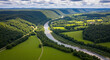 © Attaul - Aerial view of a lush green valley with a winding river flowing through it on a sunny day, creating a picturesque and tranquil landscape