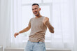 © SHOTPRIME STUDIO - Joyful man celebrating success indoors with bright sunlight pouring through the window. His energetic pose captures a sense of happiness and positivity in a modern space.