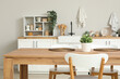 © Pixel-Shot - Wooden dining table with houseplant and wicker mats in stylish kitchen