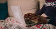 © ABCreative - A close-up of the hands of a young man of multi-ethnic background typing on a laptop keyboard. Dressed in a warm holiday sweater with a watch on his wrist and a ball earring, he concentrates on his