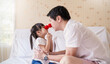 © paulaphoto - Portrait of playful moment between father and young daughter touching red clown noses while sitting together on a bed at home. Father’s day