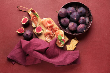 Wall Mural - Wooden board of bread slices with delicious prosciutto and fresh fig on red background