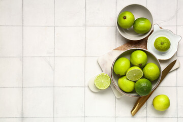 Wall Mural - Bowls with fresh ripe limes and juicer on white tile background