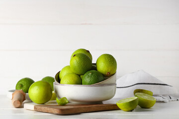 Wall Mural - Bowl with fresh ripe limes on white wooden background