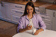 © Pixel-Shot - Young woman with glass of milk using mobile phone in kitchen at night