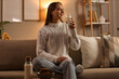 © Pixel-Shot - Young woman with glass of milk sitting on sofa at home late in evening