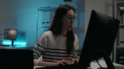 Focus Asian woman wearing glasses typing on a computer keyboard. Software engineer programming code, game design, web development. Programmer working overtime on a complex technology project at night