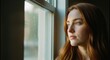 © Meow Creations - Serene young woman with beautiful red hair quietly observing outside from a sunlit window