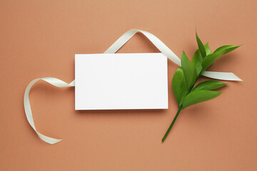 Wall Mural - Beautiful ribbon, blank card and green leaves on beige background, flat lay