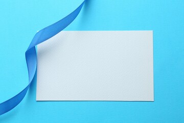 Wall Mural - Beautiful ribbon and blank card on light blue background, flat lay
