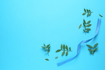 Wall Mural - Beautiful ribbon and green leaves on light blue background, flat lay. Space for text