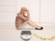 © Ljupco Smokovski - Sad mature woman sitting on the ground with a weight scale and measure tape