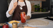 © VictorCanalesStudio - Woman in apron spreading tomato sauce on pizza dough in a modern kitchen