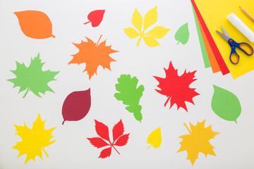 Wall Mural - Created colorful different paper leaves. Application paper, scissors, glue stick and pencil on light gray table background. Closeup. Making autumn decoration. Top down view.