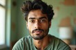 © Vadym - Young man with dark wavy hair and beard gazes ahead, relaxed expression. Casual green t-shirt worn, soft blurred background indoors. He looks thoughtful and approachable.