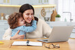 © New Africa - Smiling woman working with laptop and her son at wooden desk in home office