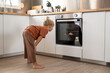 © sutulastock - Curious young boy in brown clothes bending forward and looking into oven while waiting for food to bake in modern bright kitchen