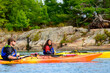 © Michael Connor Photo - Sea kayaking expedition on Georgian Bay in fall: a young woman and a young man  pause on the water with rocks and boreal forest in background room for text