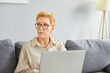 © Studio Romantic - Portrait of confident senior woman using laptop sitting on couch in the living room at home. Concept of e-learning for mature people or distance freelance work career for retirement.