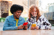 © Jose Calsina - Two cheerful young women are enthusiastically using their smartphones, sharing a joyful experience as they engage with mobile applications, immersed in technology and connection with each other.