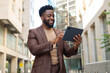 © Dexon Dee - Happy black businessman using tablet in city street