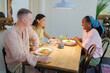 © aerogondo - Three friends having conversation during lunch at a cozy restaurant in the afternoon with a young African woman wearing a blue scarf