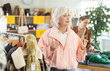 © JackF - Elderly woman with gray hair and wearing a pink jacket at a sale of outerwear and warm clothes for the winter. Customers stand in the store and choose clothes for autumn